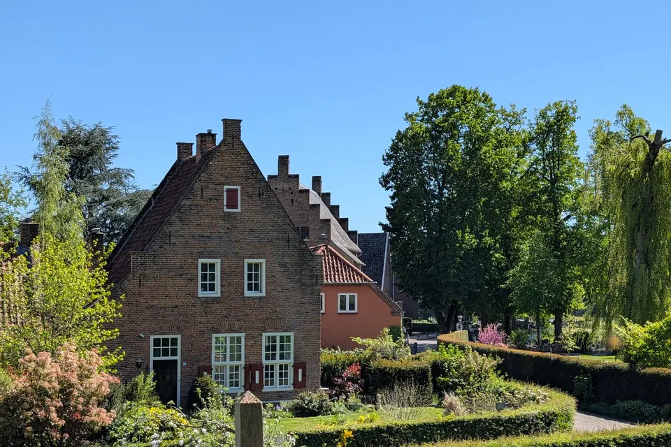 Bakstenen woonhuis met trapgevel in een voorjaarstuin met hagen