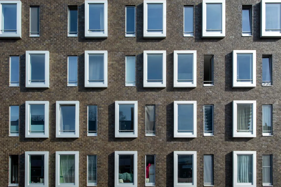 Gevel van een modern woongebouw van donkere baksteen met witte raamkozijnen